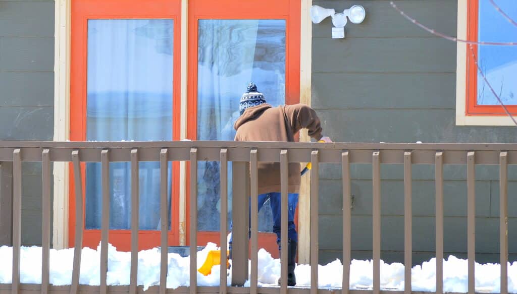 Female shoveling snow off patio deck outside.