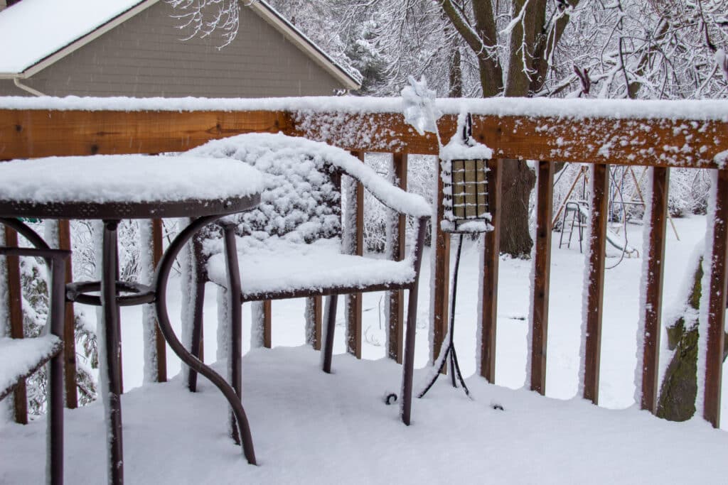 Close up view of an outdoor Home Deck and Furniture containing a round table and chairs, covered with thick snow during a winter blizzard