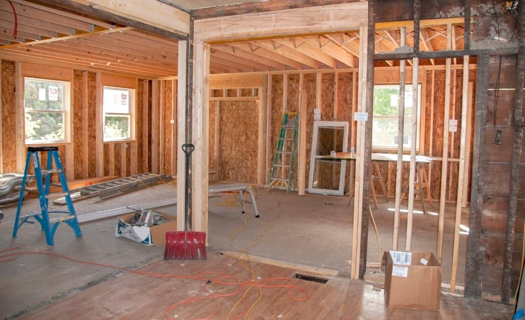 Construction site of room additions with wooden studs and exposed insulation, featuring various construction tools, and natural light streaming in through windows.